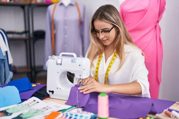 Elbise dükkanında dikiş makinesi kullanan kendine güvenen genç sarışın kadın terzi.