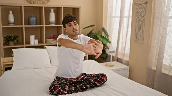 年轻英俊的他的惊慌失措的男人享受着一个平静的早晨 穿着睡衣坐在床上 舒舒服服地张开双臂 在家里的卧室里保持健康和放松 — 图库照片