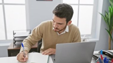 Modern ofis ortamında dizüstü bilgisayarında çalışan odaklanmış, sakallı bir İspanyol adam profesyonelliği ve konsantrasyonu temsil ediyor..