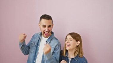 Kot gömlekli güzel çift kazandı! Heyecanlı, pembe soyutlanmış arka planda dikilmiş zafer jestleri yapıyor ve sevinç çığlıkları atıyordu..