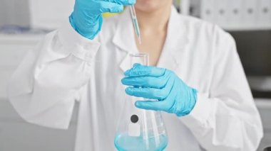 Bir kadın bilim adamı laboratuarda bir deney yapıyor. Mavi bir sıvıyı hacimli bir şişeye yerleştiriyor..