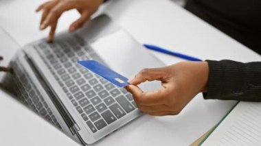 Ofiste dizüstü bilgisayar kullanırken elinde kredi kartı tutan bir kadın online alışveriş veya dijital bankacılık tasvir ediyor..
