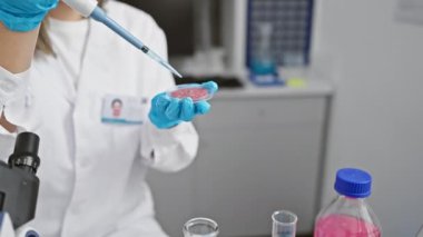 Laboratuvarda genç bir İspanyol kadın bilim adamı mikroskop yakınında bir petri kabı ve pipetle deneyler yapıyor..