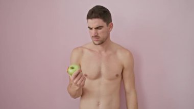 Kendinden emin, genç İspanyol erkek, gururla bir elma tutuyor ve pembe izole bir arka plan üzerinden kameraya pozitif ışık saçıyor. Çenen dinleniyor, kolların çapraz..