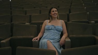 Genç bir kadın karanlık bir tiyatroda tek başına oturuyor, geniş koltuklarda gülümsüyor, zarafet saçıyor..