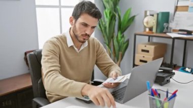 Modern ofis ortamında hesap makinesi ve dizüstü bilgisayarla finans hesapları yapan yakışıklı bir İspanyol.