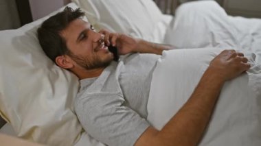 Genç İspanyol bir adam yatakta uzanıp telefonla konuşuyor. Yatak odasında dinleniyor..