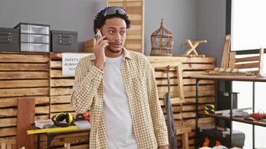 Güvenlik gözlüklü, kareli gömlekli, kapalı mekanda çalışan Afrikalı Amerikalı bir adam telefonda.