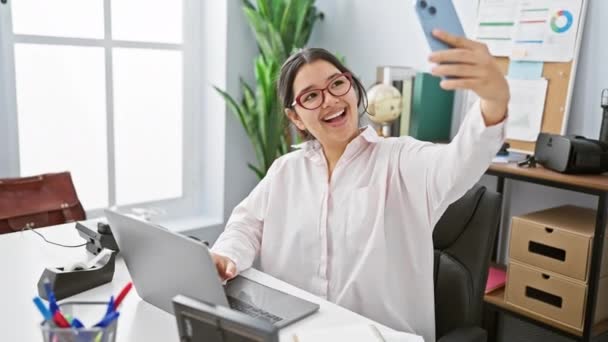 一位面带微笑的年轻女子穿着眼镜和白衬衫 在办公室里拿着手机自拍 — 图库视频影像