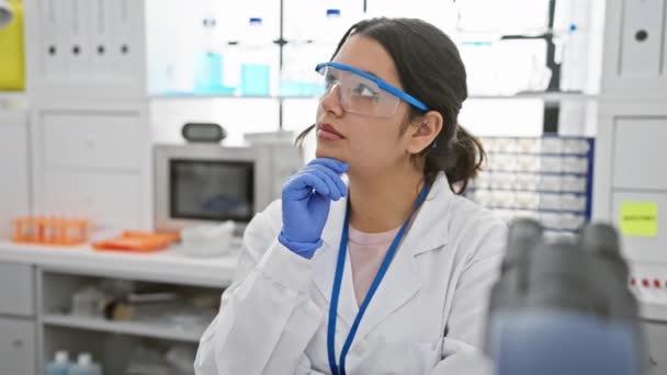 在实验室里沉思的年轻的惊慌失措的女科学家 面容严肃 手下留情 头脑发热 戴着安全眼镜 一副疑神疑鬼的画像 — 图库视频影像