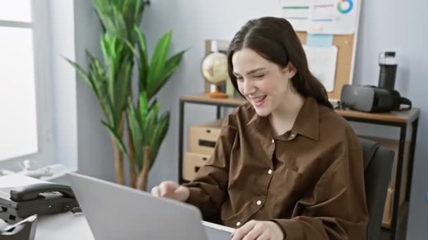茶色のシャツを着た若い女性は ラップトップ 携帯電話 植物の装飾で彼女の近代的なオフィスでリラックスしています — ストック動画
