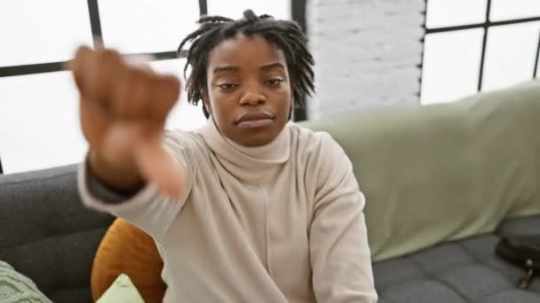 年轻的黑人妇女 坐在舒适的沙发上 怒气冲冲地垂下大拇指 不喜欢有不愉快表情的概念 — 图库视频影像