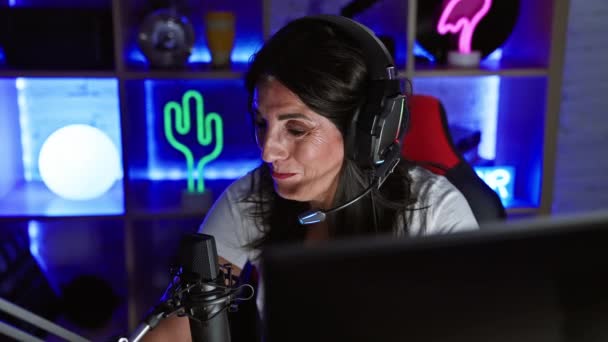 Reife Frau Trägt Kopfhörer Mit Mikrofon Einem Neonbeleuchteten Spielzimmer Der — Stockvideo