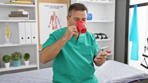 Ώριμος Άντρας Ποδιά Πίνει Καφέ Και Τσεκάρει Smartphone Ιατρείο — Αρχείο Βίντεο