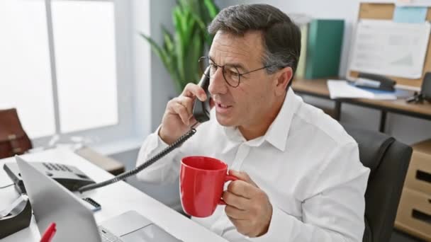 中年のビジネスマンが電話で話し 近代的なオフィスの設定で赤いマグカップを保持 — ストック動画