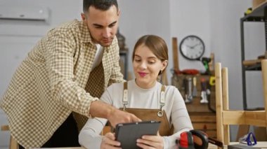 Bir erkek ve kadın, iyi donanımlı bir marangozluk atölyesinde tablet kullanarak iş birliği yapıyorlar..