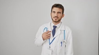 Kendinden emin bir şekilde poz veren genç ve modaya uygun İspanyol adam neşeli bir gülümsemeyle saçlarına dokunuyor. Steteskop takıyor, çekici ve neşeli bir şekilde dikiliyor izole edilmiş beyaz bir arka plana karşı..