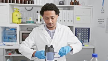 Laboratuvar önlüklü genç adam araştırma ve sağlık hizmetlerini temsil eden bir laboratuvar ortamında mikroskop kullanıyor..