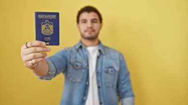 Genç Arap adam elinde dur işareti, elinde emirlik pasaportu, sarıya ciddi bir bakış, izole bir arka plan. Savunma jestine güveniyor, herhangi bir sınırı reddediyor..