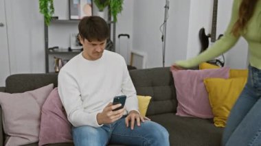 Gülümseyen bir kadın telefonuyla dikkati dağılmış bir adama sataşıyor, rahat bir oturma odasında beraberliği yakalıyor..