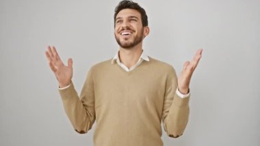 Galibiyeti sevinçle kutlayan süveter giyen, zafer dolu gülümsemeyle mutluluk saçan, beyaz arka planda izole bir şekilde duran başarılı İspanyol genç adam.