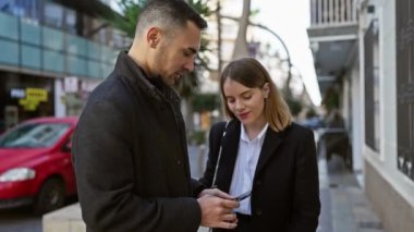 Bir kadın ve bir erkek, bir şehir caddesinde akıllı bir telefonla iletişim kuruyor ve modern bir şehir hayatı sürüyor..