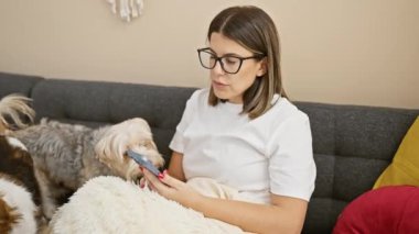 İspanyol kadın oturma odasında akıllı telefon kullanırken köpeklerle kanepede dinleniyor..