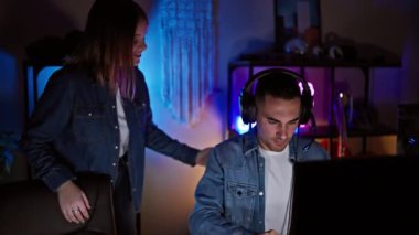 Bir kadın ve bir erkek loş bir oyun odasında bilgisayar ekranı önünde bir anlık eğlence ve takım çalışması paylaşıyorlar..