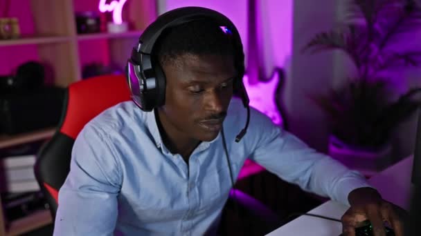 有重点的非洲男人 晚上在一个充满活力的游戏室里用电脑 带着耳机 — 图库视频影像