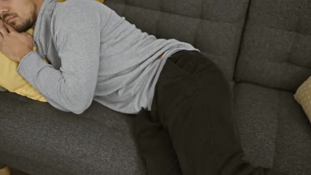 居心地の良い家の設定で緑と黄色のクッションと灰色のソファで昼寝する若い男 — ストック動画