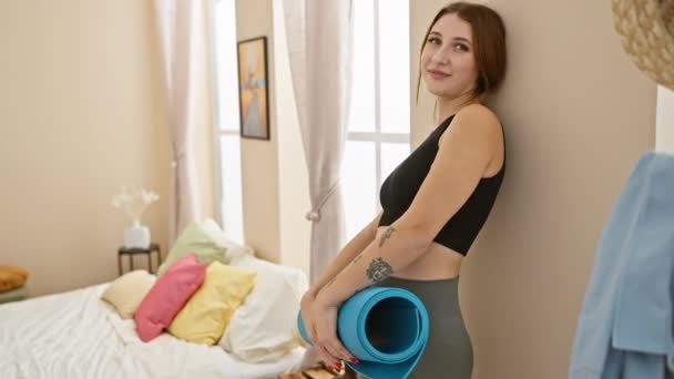 微笑的女人拿着瑜伽垫 准备在卧室里做运动 背带着窗帘和彩色枕头 — 图库视频影像
