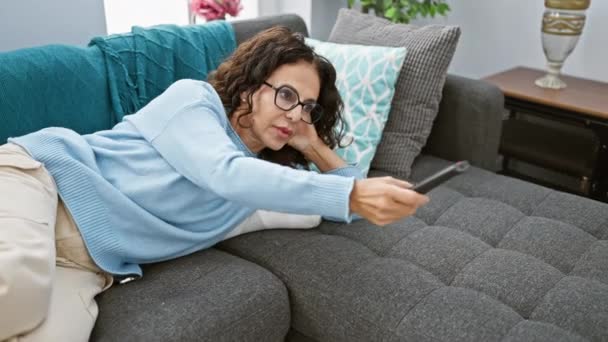 Hispanische Frau Auf Sofa Wohnzimmer Mit Fernbedienung Brille Lächelnd Entspannt — Stockvideo
