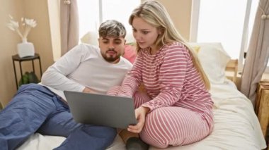 Pijamalı bir çift, rahat bir yatak odası ortamında dizüstü bilgisayar kullanıyor. Öylesine tartışıyorlar..