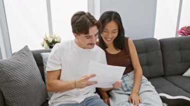 Irklar arası bir çift, İspanyol bir adam ve Asyalı bir kadın, rahat bir oturma odasındaki kanepede birlikte bir belgeyi zevkle incelerler..