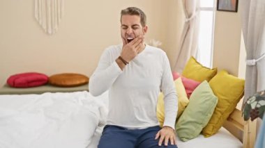 Beyaz gömlekli İspanyol adam renkli yatak odasında akıllı telefon kullanıyor.