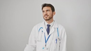 Yakışıklı, doktor ceketli, İspanyol bir adam sevinçle kendinden emin bir bakışla mesafeyi arıyor. Elinde steteskop, beyaz izole bir arka plana bakıyor..