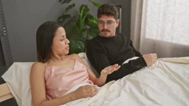 Bir kadın ve bir erkek yatakta otururken sohbet ediyorlar, bir çiftin yatak odasındaki yaşam tarzını resmediyorlar..
