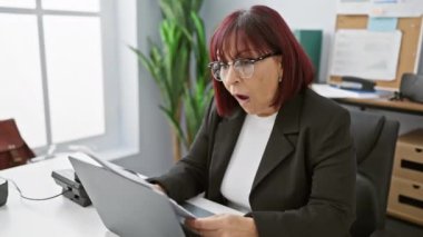 Parlak bir ofiste belgelerle çalışan olgun bir İspanyol iş kadını başarıyı ifade eder