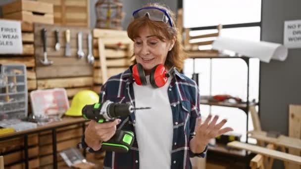 ジョイフルな中年の女性大工は ビームの笑顔でエキサイティングな勝利を祝い 自信を持って大工のワークショップで彼女のドリルを振る — ストック動画