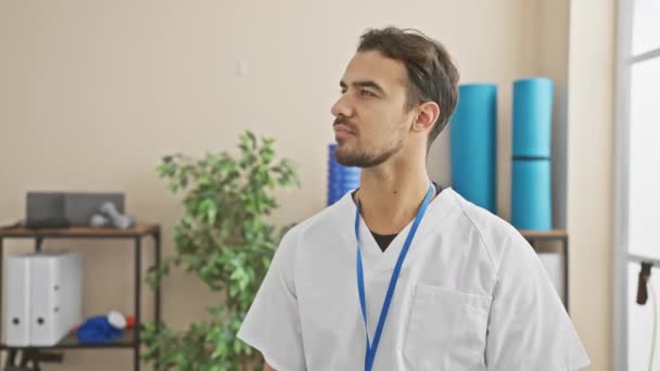 医療ユニフォームの自信を持ったヒスパニックの男性は 医療従事者や職場環境を代表するクリニックに立っています — ストック動画