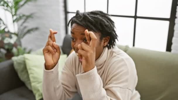 一位头发蓬乱的年轻黑人妇女坐在室内沙发上兴奋地交叉着她的手指 表现出她的期望或希望 — 图库视频影像
