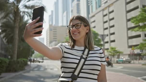 여자는 손바닥 나무와 마천루로 두바이 거리에 스마트 폰으로 셀카를 찍는다 — 비디오