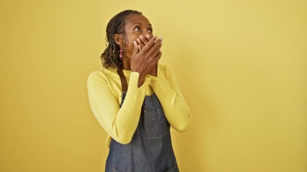 エプロンの驚異的な中年アフリカ系アメリカ人女性がショックで口を覆う 隔離された黄色の背景に秘密として保持されていない間違い — ストック動画