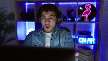 Oyun odasında kulaklığı olan sıkıntılı bir adam gece boyunca bilgisayar ekranından rahatsız görünüyor..