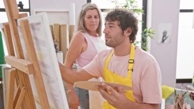 İki gülümseyen sanatçı, bir erkek ve bir kadın, güvenle sarılıp çiziyorlar, bir sanat stüdyosunda yaratıcılıklarını sergiliyorlar.