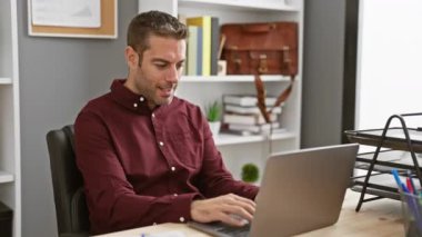 Heyecanlı genç İspanyol adam ofiste, mutlu bir şekilde zaferi kutluyor bilgisayarda kendine güvenen gülümsemesi ve zafer ifadesiyle.