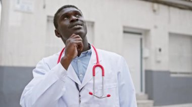 Steteskoplu doktor ceketli düşünceli bir Afrikalı kliniğin önünde duruyor..