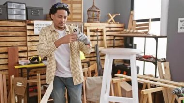 Afrika kökenli Amerikalı bir adam kafasında güvenlik gözlükleri olan iyi donanımlı bir marangozluk atölyesinde beyaz bir sandalyenin fotoğrafını çekiyor..