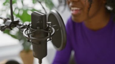 Radyodaki mikrofonun yanında gülümseyen mor elbiseli Afrikalı Amerikalı kadın..