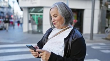 Şehrin hareketli sokağında akıllı telefon kullanan olgun bir kadın.